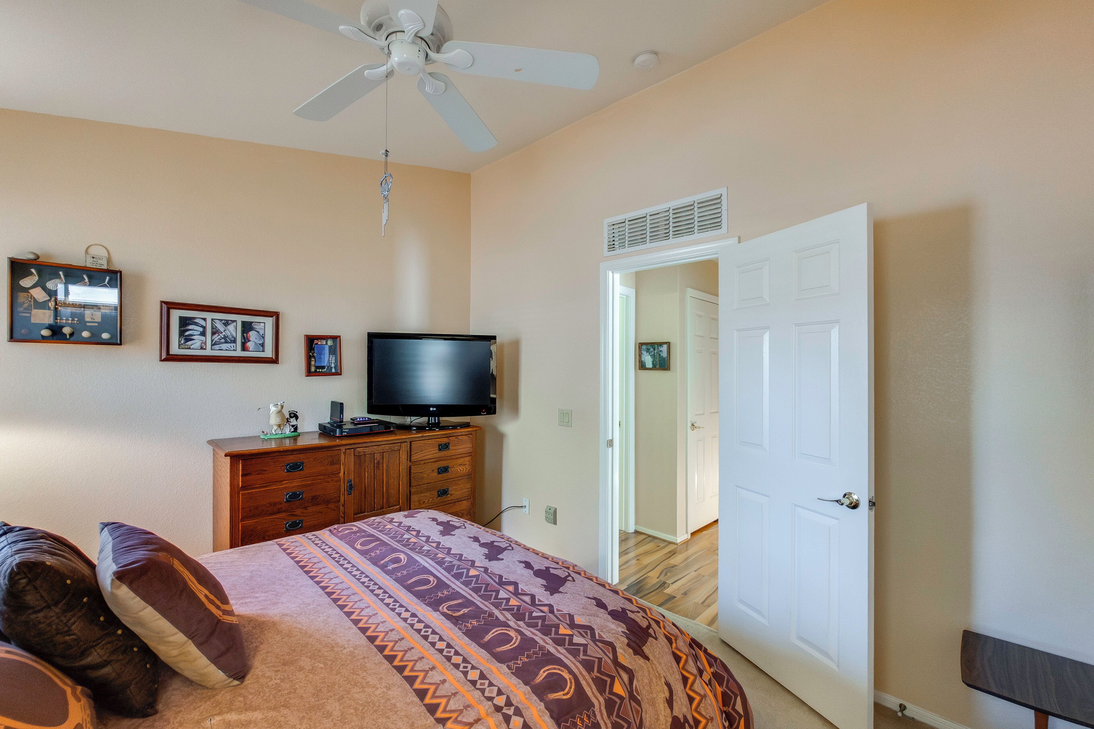 Un dormitorio con cama, televisor, ventilador de techo, cómoda y puerta que da a otra habitación.
