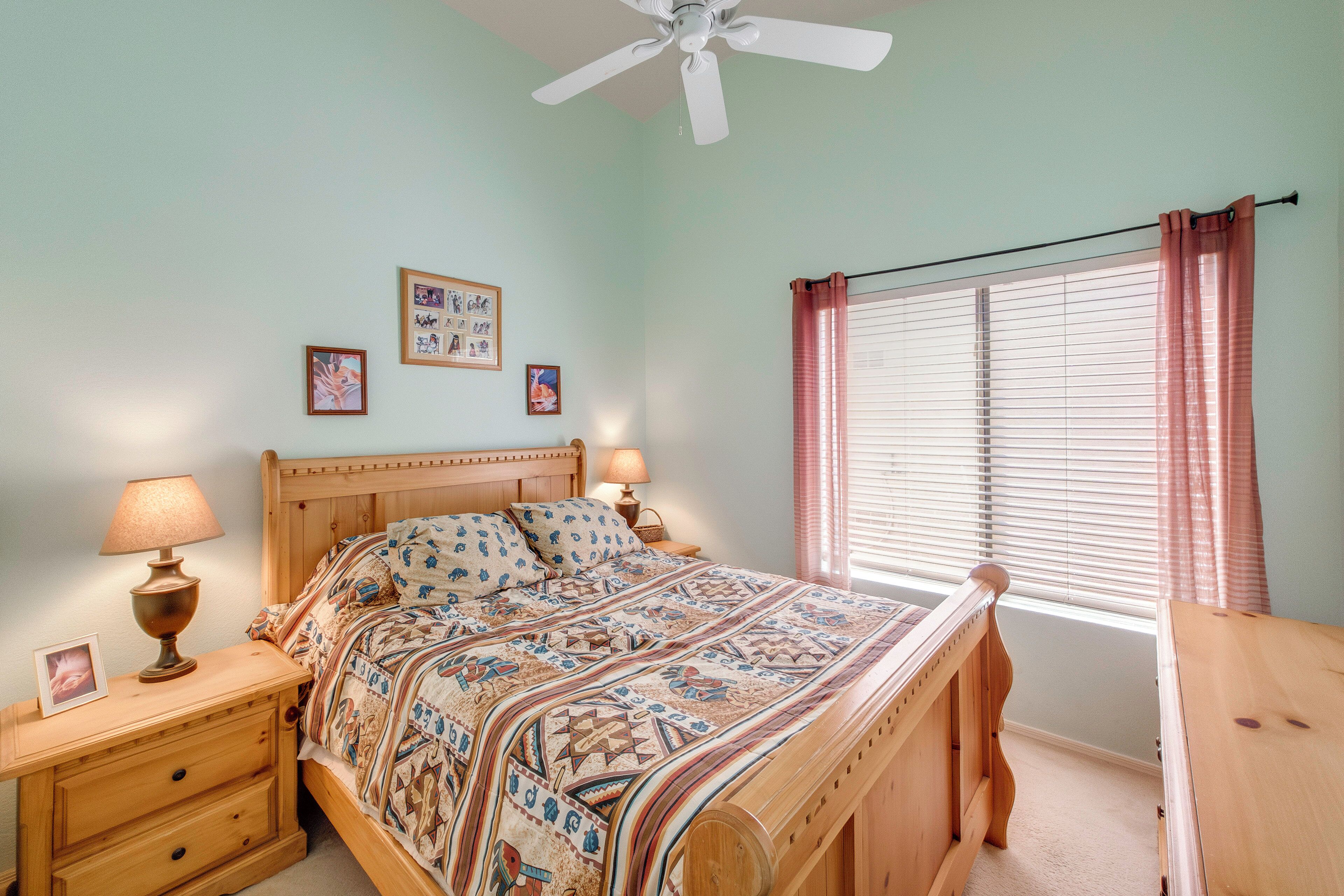 A bedroom with a bed, nightstands, a ceiling fan, a window with blinds, and wall decorations.