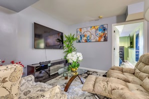 Ein Wohnzimmer mit Flachbildfernseher, Glastisch, beigem Sofa und Couch mit Blumenmuster.