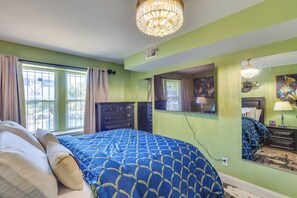 Ein Schlafzimmer mit Bett, einer Kronleuchter, einem Schminktisch, einem Spiegel und einem Fenster mit Vorhängen.
