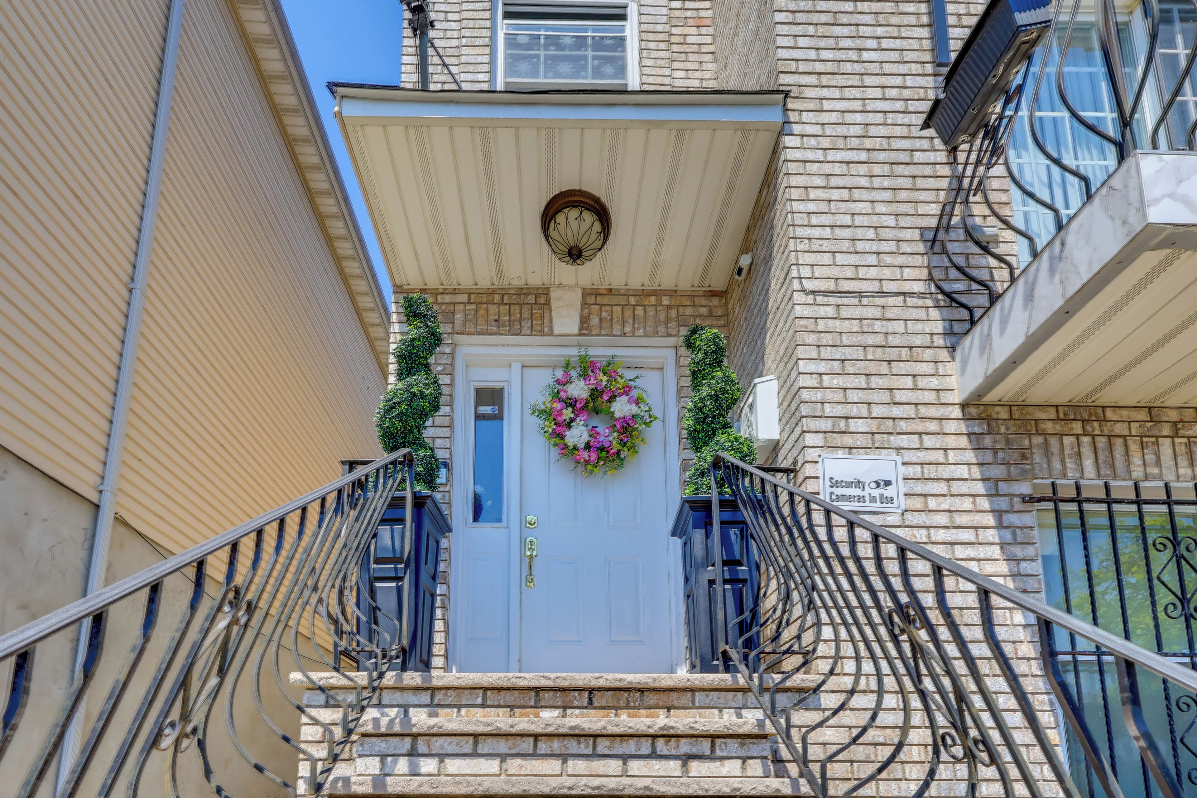 A building entrance with a white door, a security camera sign, and a decorative wreath.