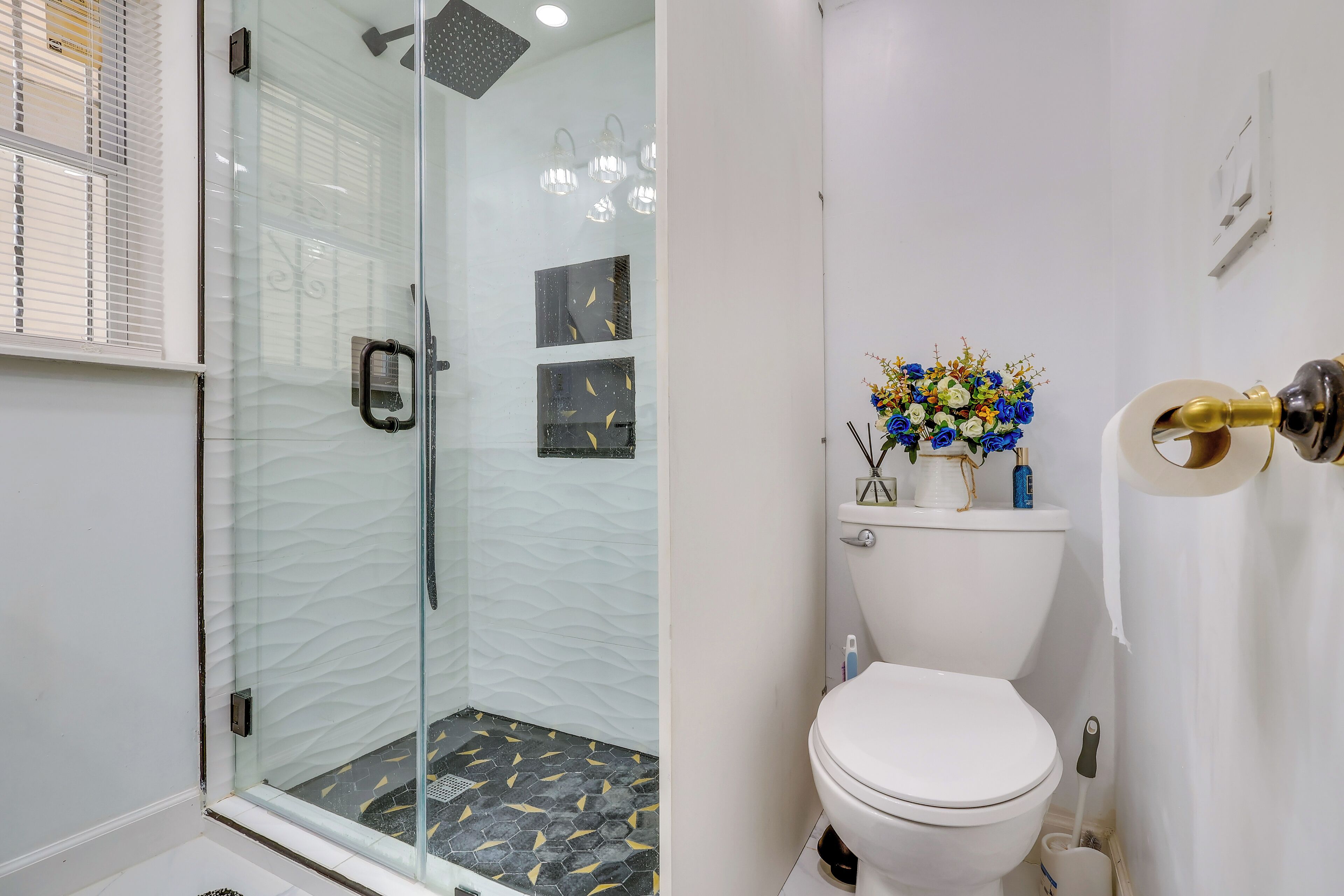 A bathroom with a glass-enclosed shower, a toilet, and a decorative vase with flowers.