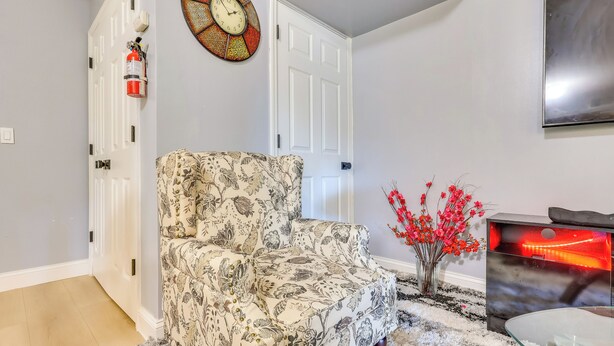 A living room with a patterned armchair, a decorative clock, a vase with red flowers, and a fireplace. - Walkable Extended Base 2 Mi to Dtwn & Penn Station (Newark)