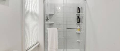 A corner shower with a glass door, white tiled walls, a white towel hanging on the door, and a toilet to the left.