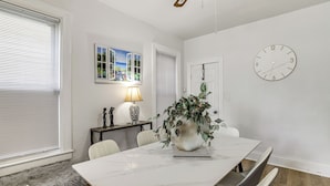 A dining area with a marble table, chairs, a potted plant, a clock, and a window with blinds. - Stroll to Falls & Seneca Casino! Family Getaway (Niagara Falls)