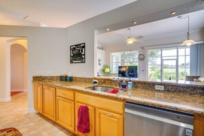 A modern kitchen with granite countertops, wooden cabinets, a dishwasher, and a large window offering a view. - Pool Access & Lake-view Lanai! Port Charlotte Gem (Port Charlotte)