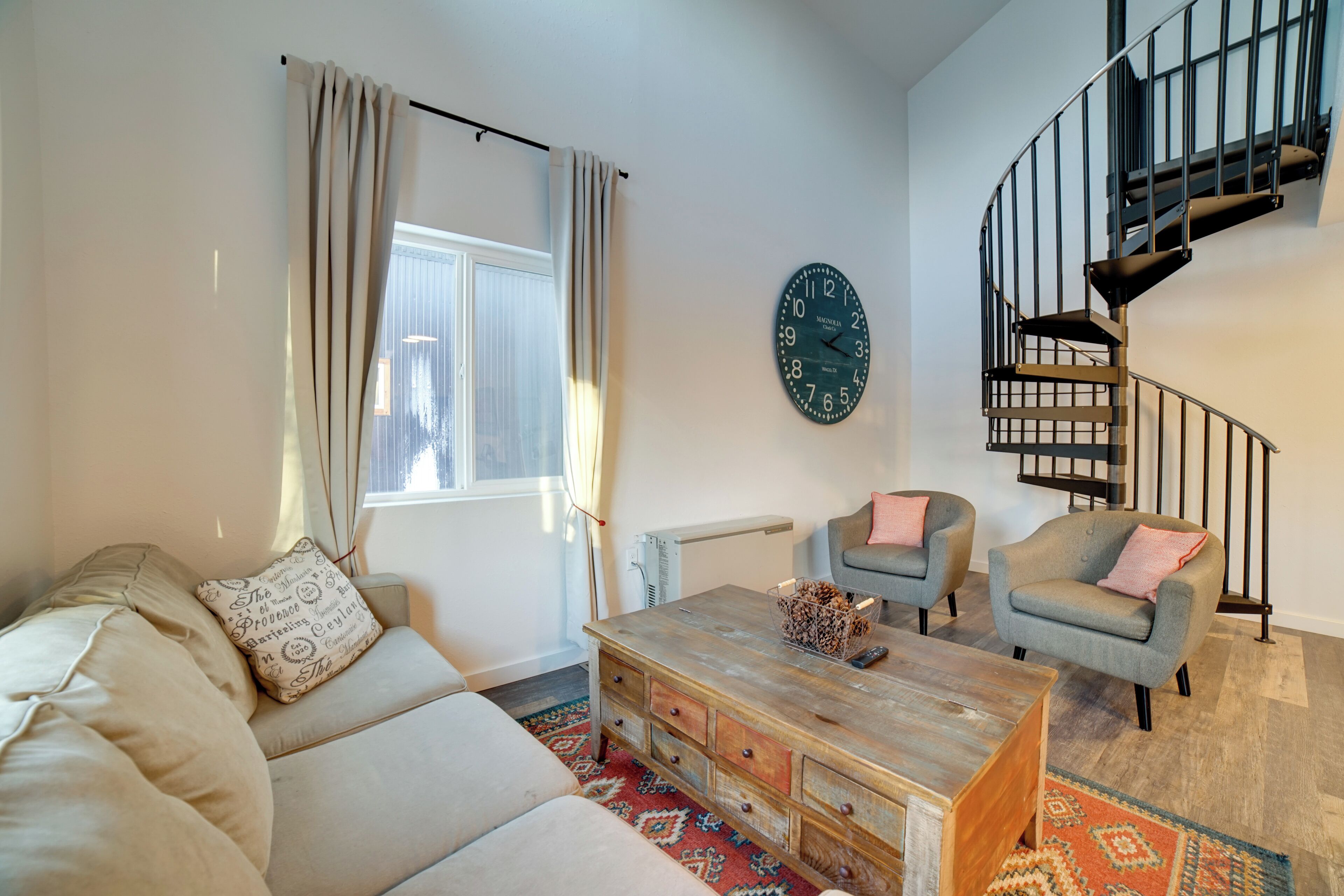 A living room with a sofa, armchairs, a coffee table, a clock, and a spiral staircase.