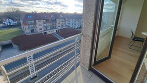 A balcony with a view of residential buildings, a railing, and a door leading to a room with a chair and a table. - Sunny Apartment Near the Beach (Koksijde)