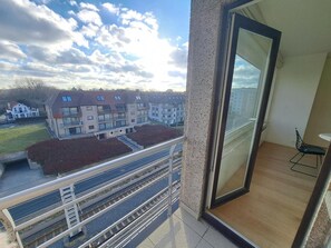 Ein Balkon mit Blick auf Wohnhäuser, einem Geländer und einer Tür, die in einen Raum mit Stuhl und Tisch führt.