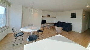 A modern living space with a dining area, a sofa, and a TV. - Sunny Apartment Near the Beach (Koksijde)