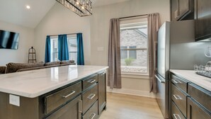 A modern kitchen with a large island, dark wood cabinets, and a view of a brick building. - Near AFB & Medical Center: Modern San Angelo Home (San Angelo)