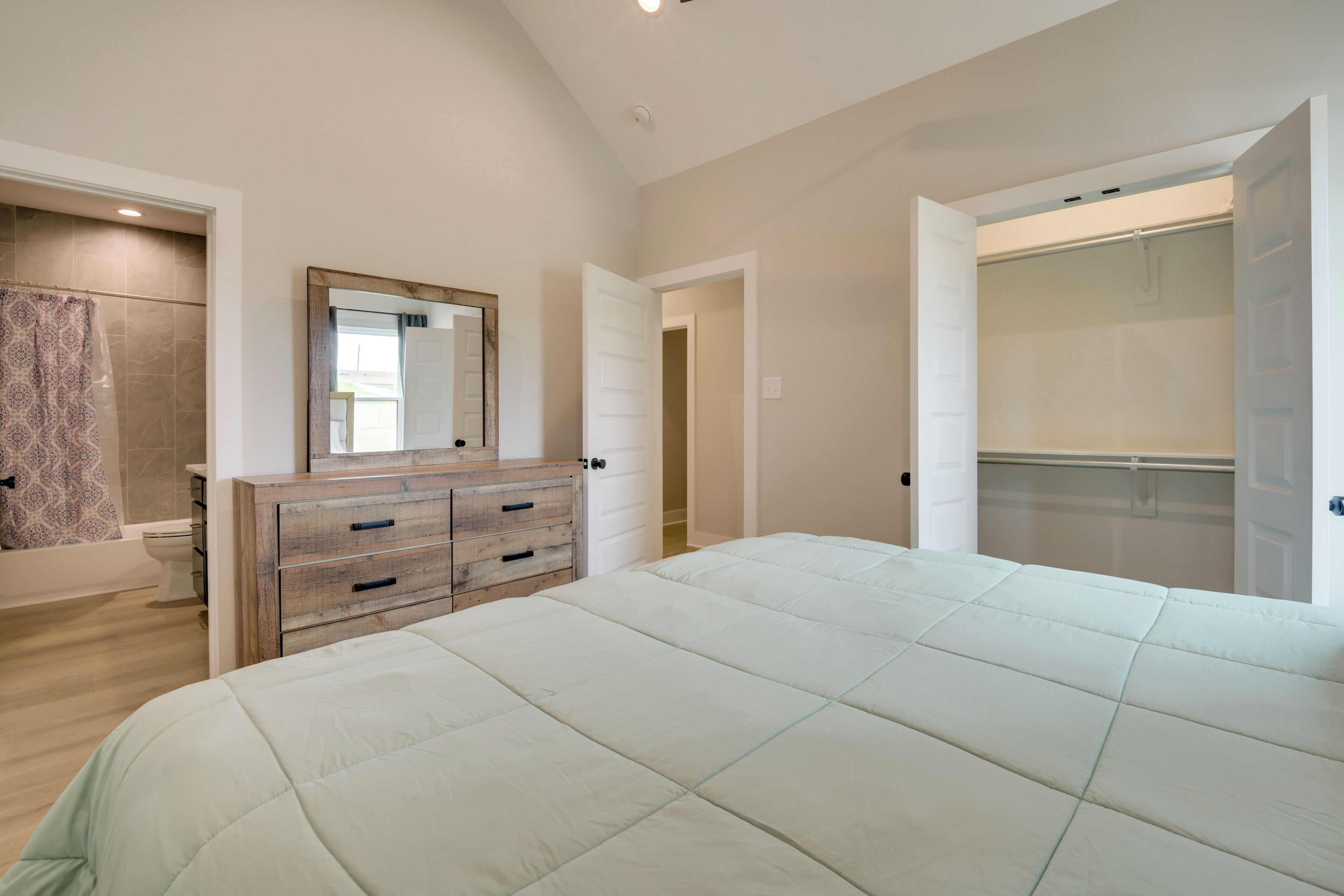 Un dormitorio con cama, cómoda, espejo y vestidor.