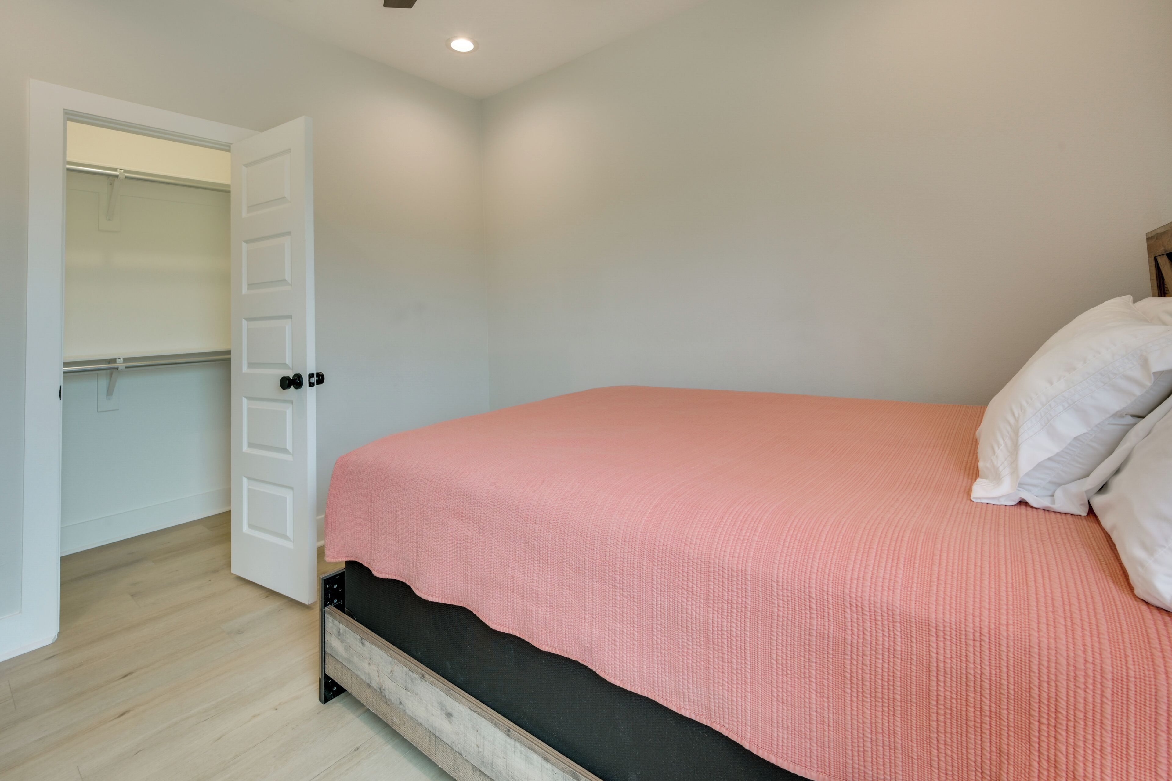 A bedroom with a bed, white walls, a wooden floor, and a closet with a door.