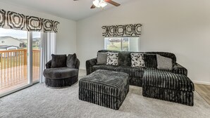 A living room with a sectional sofa, ottoman, and chair, a ceiling fan, and a view through large windows. - 4 Mi to Ellsworth Afb! Suburban Home for Families (Box Elder)