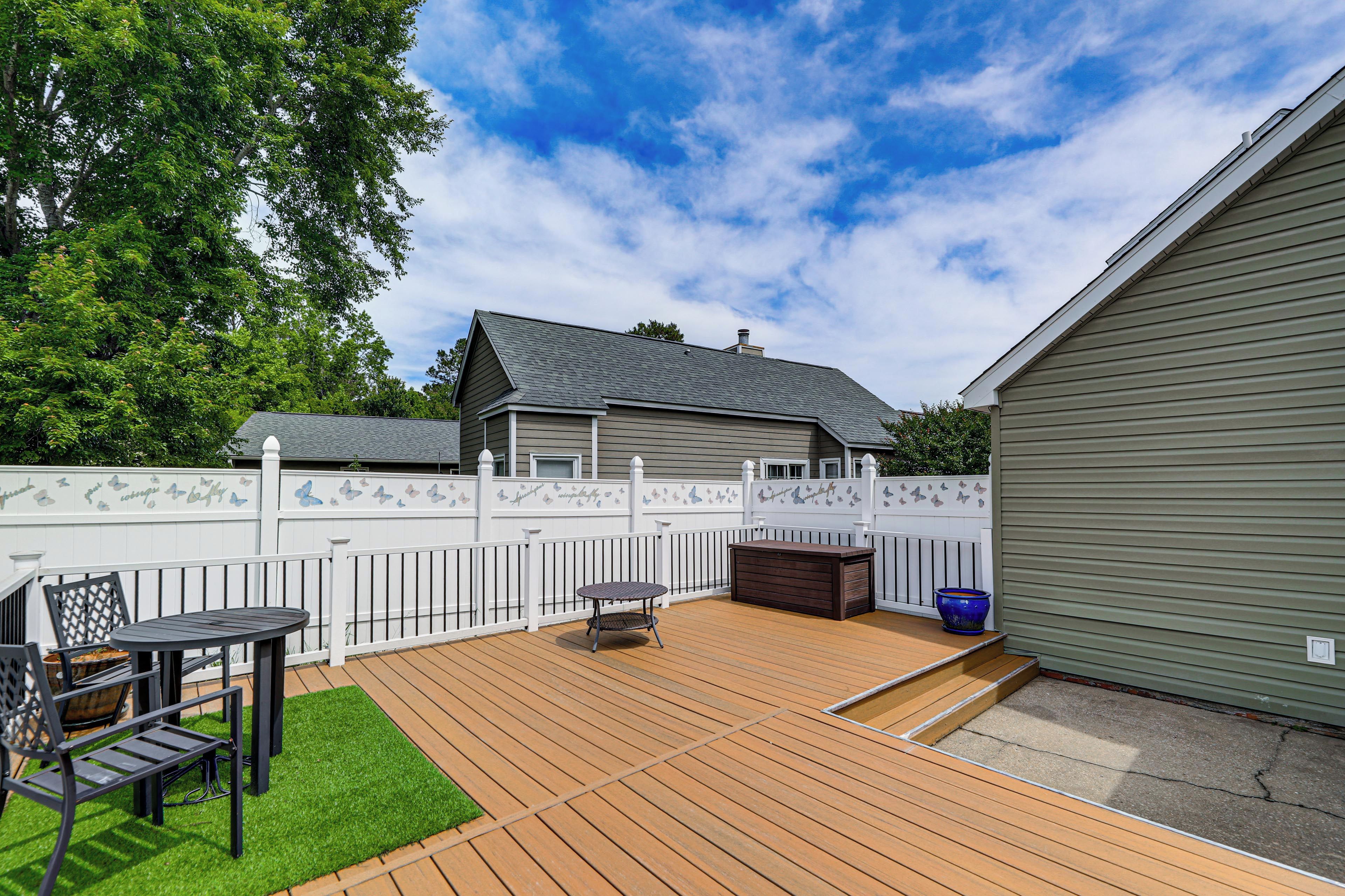 A backyard with a wooden deck, a table, chairs, a hot tub, and a fenced area.