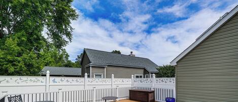 A backyard with a wooden deck, a table, chairs, a hot tub, and a fenced area.