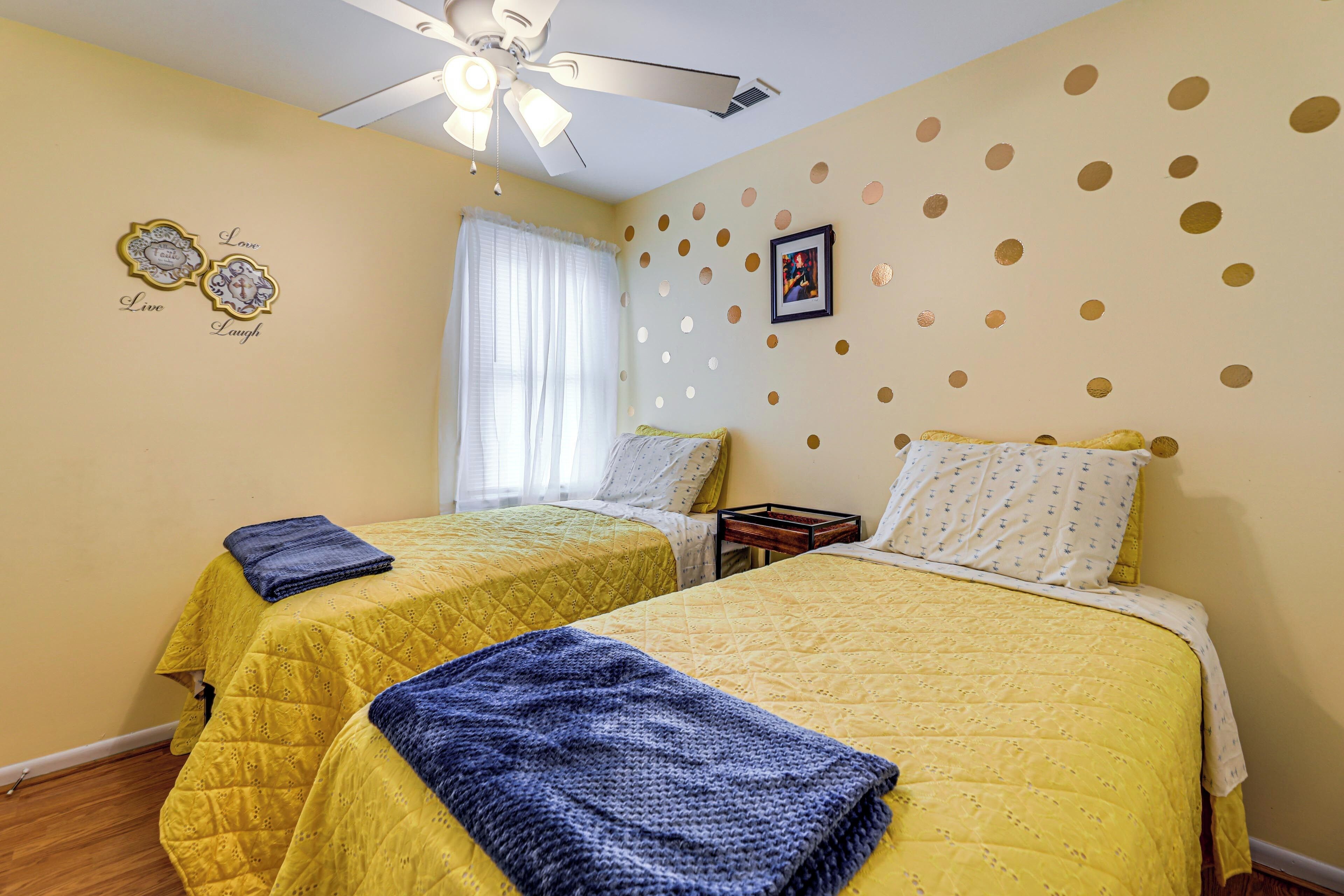 A bedroom with two beds, a ceiling fan, a window with curtains, and decorative wall stickers.