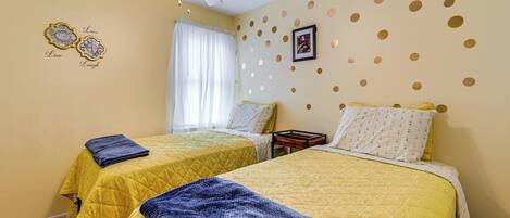 A bedroom with two beds, a ceiling fan, a window with curtains, and decorative wall stickers.