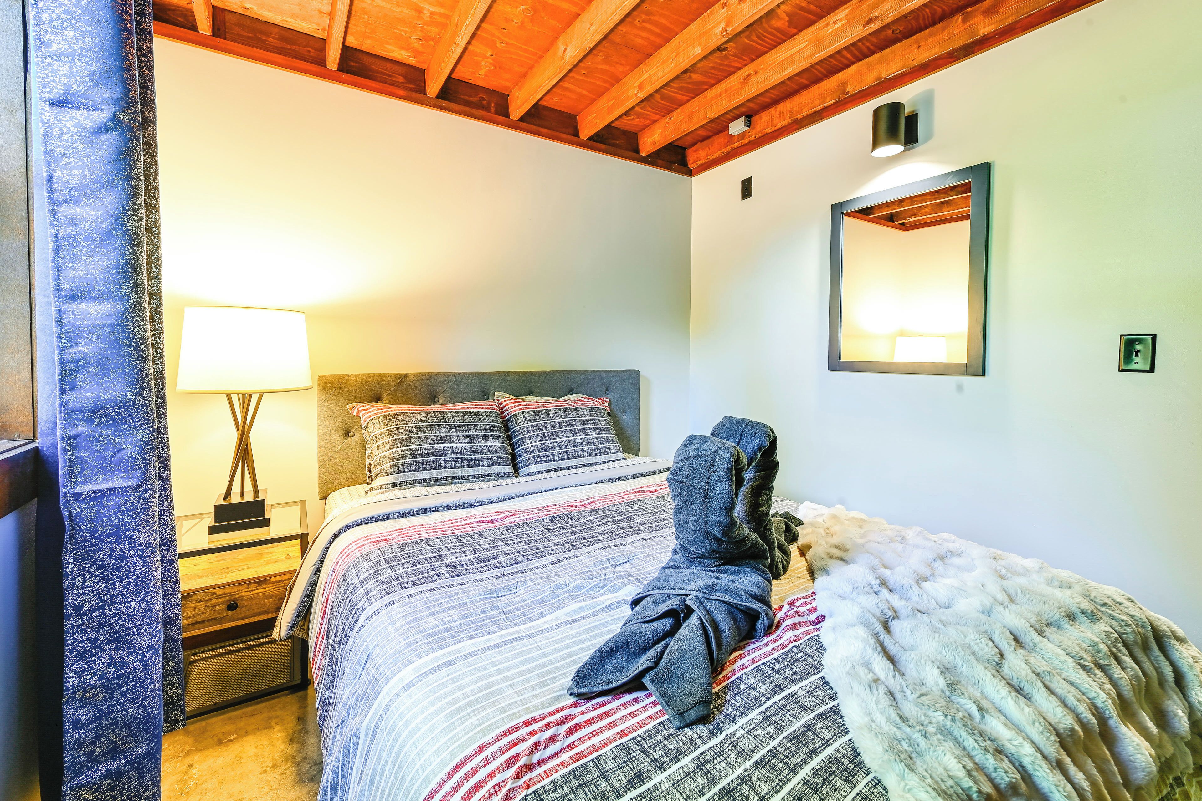 A bedroom with a bed, a nightstand, a lamp, a robe, and a mirror on the wall.