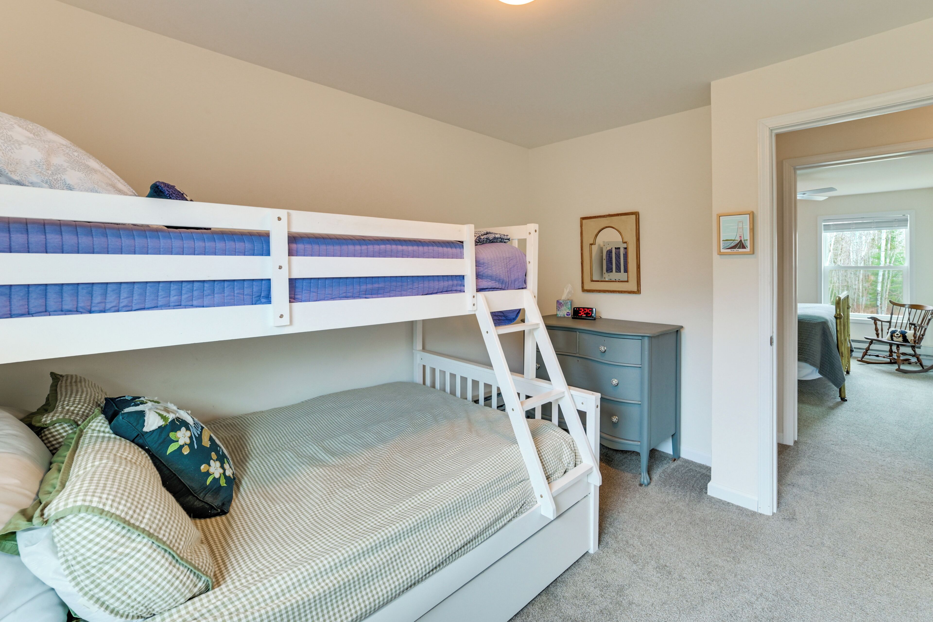 A bunk bed with a desk and chair, a small table with a picture frame, and a door leading to another room.
