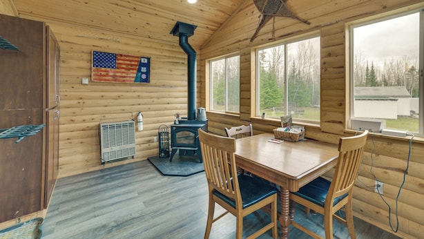 L’intérieur d’une cabane en bois, avec une table à manger, des chaises, un poêle à bois et une grande fenêtre.