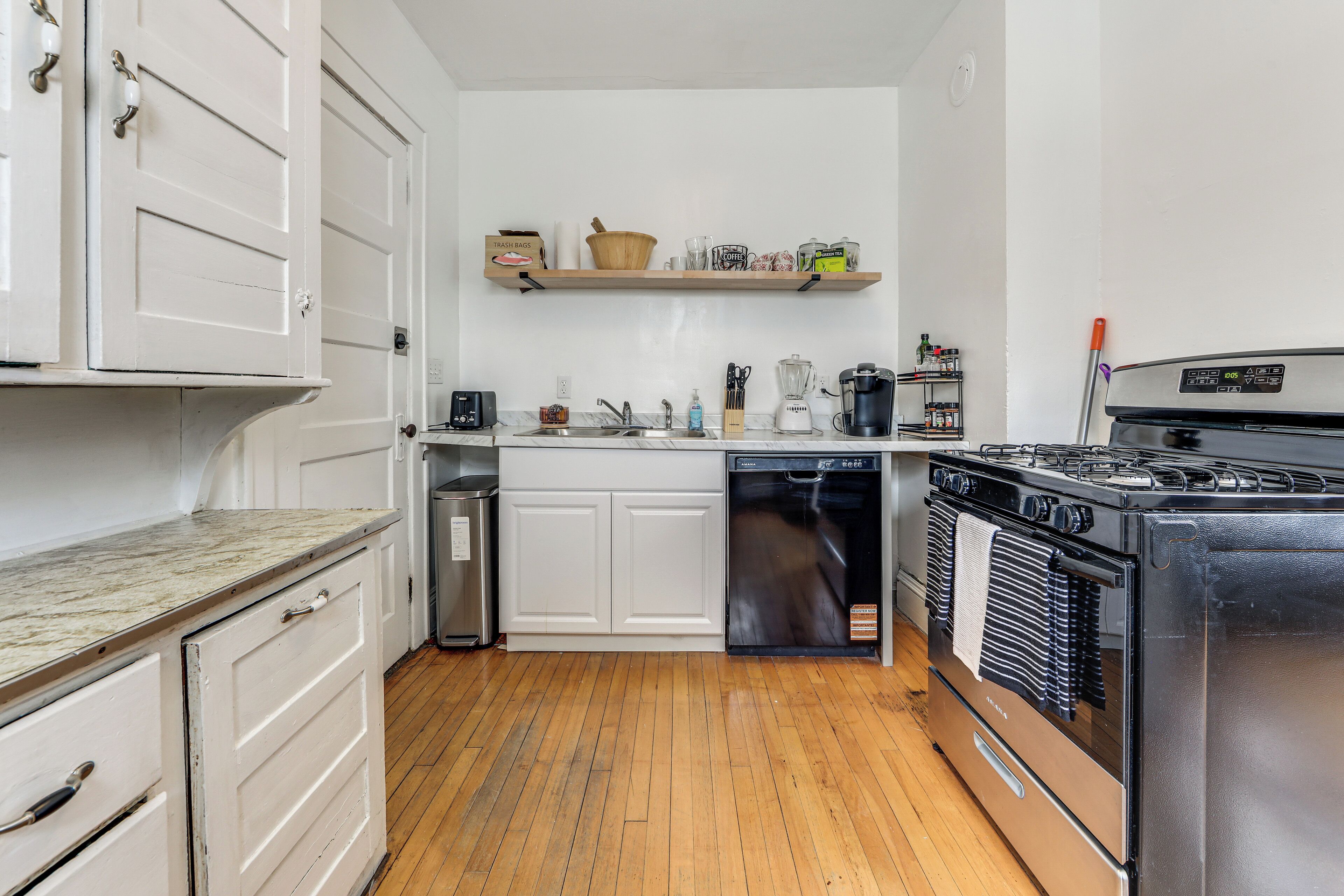 A kitchen with white cabinetry, a dishwasher, a stove, and a shelf with kitchen items.
