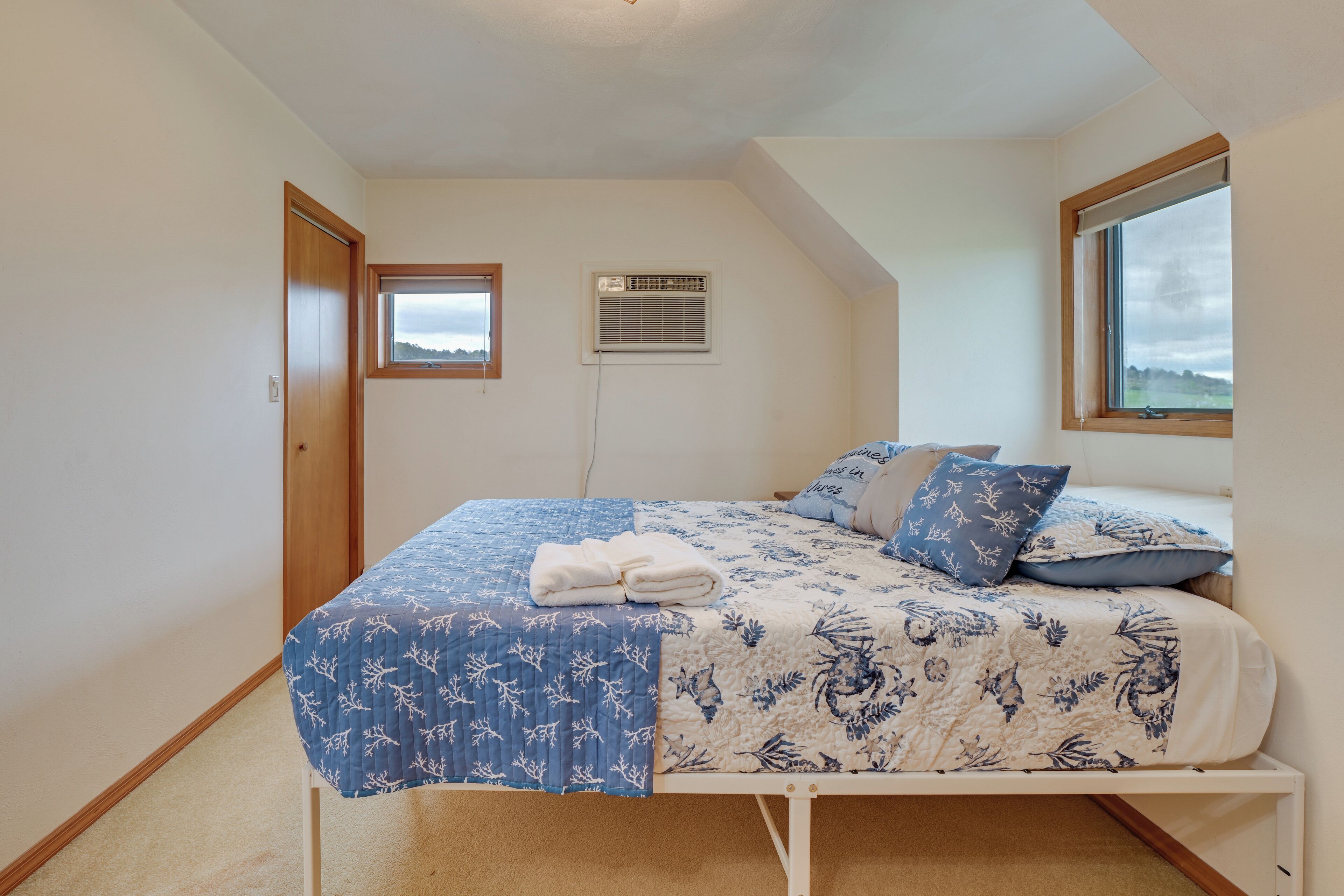A bedroom with a bed, a window, an air conditioning unit, and a door.
