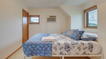 A bedroom with a bed, a window, an air conditioning unit, and a door.