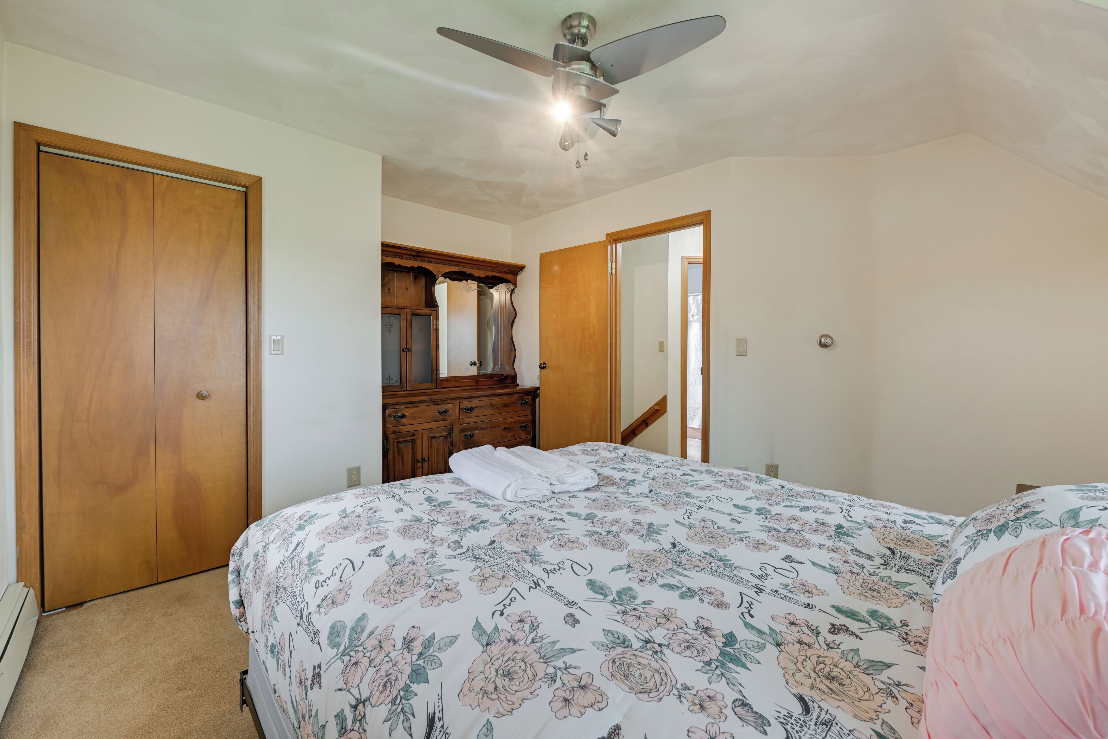 Ein Schlafzimmer mit einem Bett, einem Holzschrank, einem Schminktisch, einem Deckenventilator und einem Spiegel.