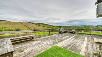 Une terrasse en bois, dotée de bancs et d’une pelouse, qui offre une vue sur un paysage vallonné.