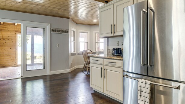 A kitchen with a stainless steel refrigerator, wooden flooring, and a view of the outdoors through a sliding glass door. - Hiking, Wineries & More! Mtn-view Gem in Tehachapi (Tehachapi)