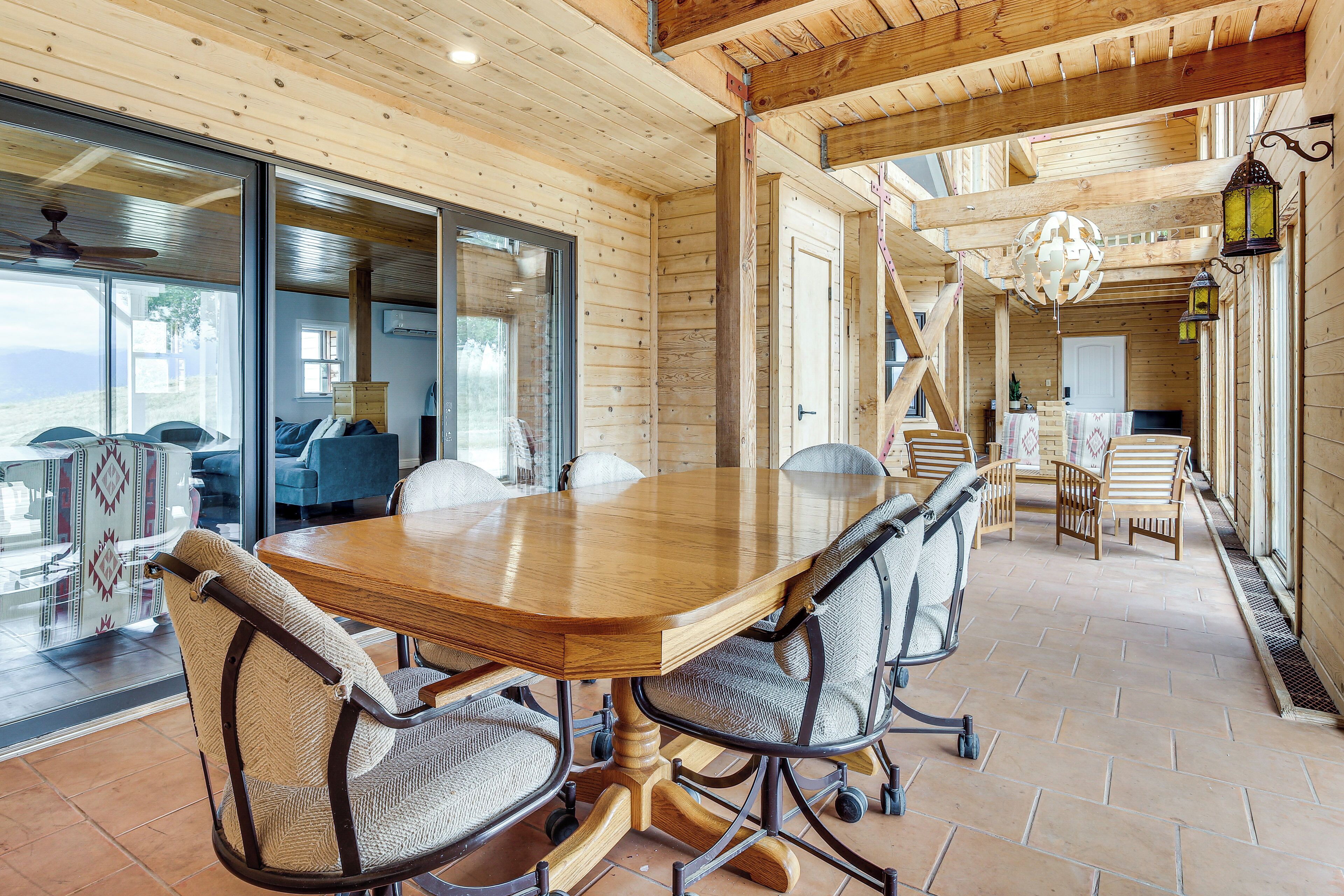 Un intérieur en bois avec une grande table à manger, des chaises et une vue sur l’extérieur, visible à travers une porte vitrée.
