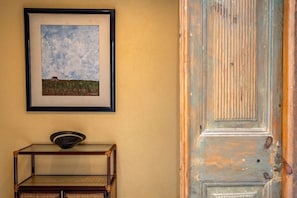 A framed landscape painting, a small wooden table with a bowl, and a weathered door. - Rustic Village Studio by the Tagus - Porto Brandão (Caparica)