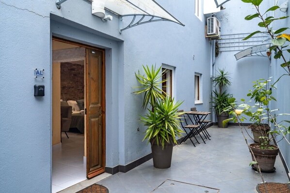 A courtyard with a wooden door, potted plants, and a small table with chairs. - Rustic Village Studio by the Tagus - Porto Brandão (Caparica)