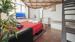 A bedroom with a bed, a desk with a computer, a chair, a staircase, and a plant. - Captivating Loft in Prime Location Near Colosseum (Rome)