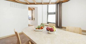 A dining area with a marble table, two white bowls with fruits and vegetables, wooden chairs, and a view of the kitchen through an open door. - Captivating Loft in Prime Location Near Colosseum (Rome)