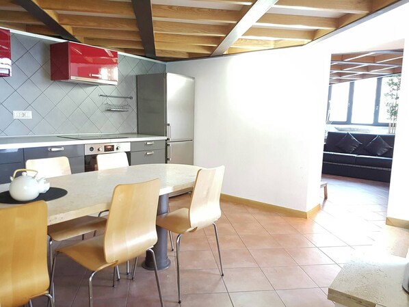 A modern kitchen with a dining area, featuring a large table, chairs, and a red cabinet. - Captivating Loft in Prime Location Near Colosseum (Rome)