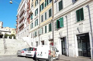A multi-story building with a staircase leading to the entrance, parked cars, and a clear sky. - Captivating Loft in Prime Location Near Colosseum (Rome)