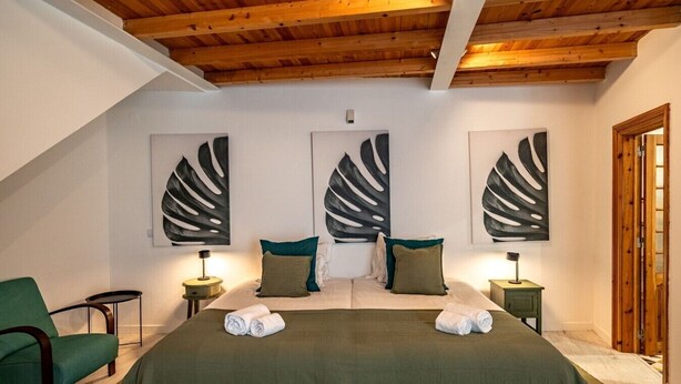 Ein Schlafzimmer mit einem großen Bett, zwei Nachttischen, einem grünen Sessel und drei abstrakten Wandbildern.