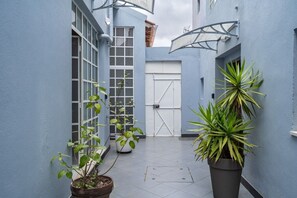 A narrow alleyway with a blue wall, potted plants, and a closed gate. - Secret Riverside Studio in Porto Brandão (Caparica)