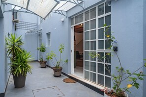 A narrow corridor with potted plants, a glass door, and a metal staircase. - Secret Riverside Studio in Porto Brandão (Caparica)