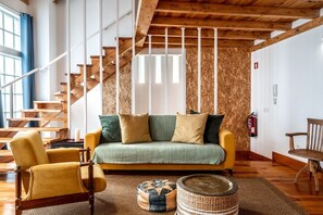 Ein Wohnzimmer mit einer Couch, einem Sessel, einem kleinen runden Tisch, einer Treppe und einem Feuerlöscher.