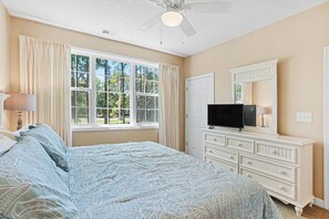 Ein Schlafzimmer mit einem Bett, einem Schminktisch, einem Fernseher und einem Fenster mit Vorhängen.