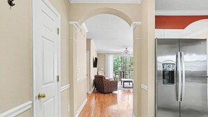 Um corredor com porta branca, cadeira estampada, frigorífico de aço inoxidável e área de jantar com mesa e cadeiras.