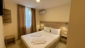 A hotel room with a bed, curtains, a television, and an air conditioning unit. - Hotel Olt by Ventura (Mamaia)