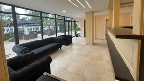 A spacious lobby with large windows, a black sofa, and a reception desk. - Hotel Olt by Ventura (Mamaia)