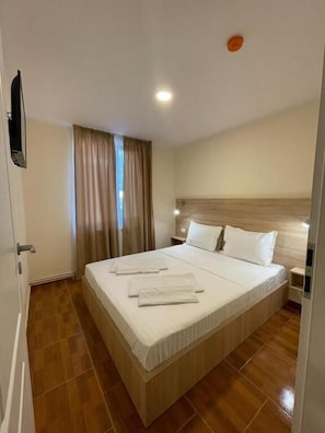 A hotel room with a large bed, wooden headboard, and a flat-screen TV mounted on the wall.
