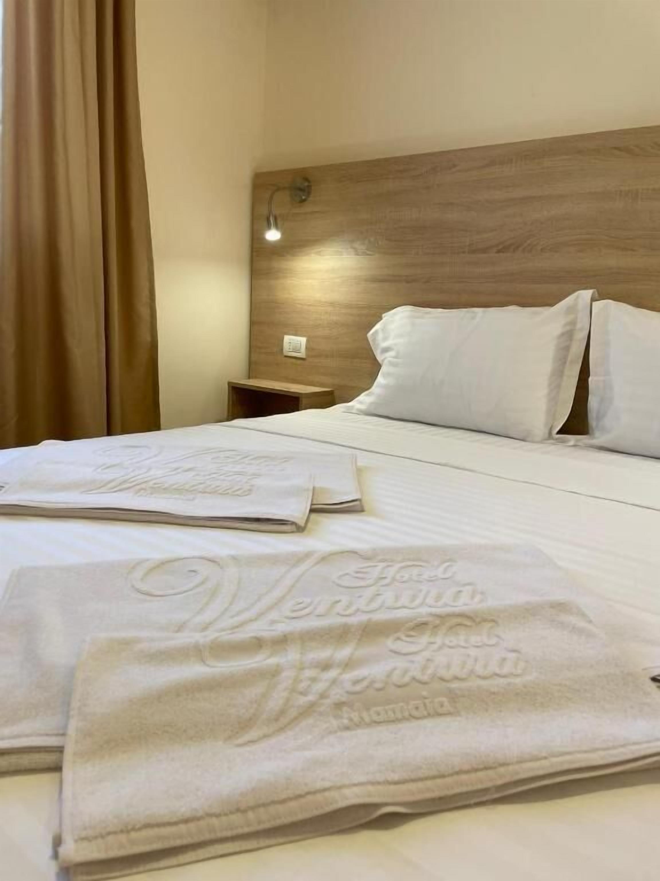 A hotel room with a wooden headboard, a bed with white linens, and two towels with embossed text.