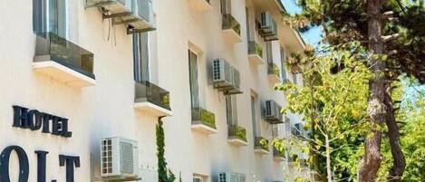 A multi-story hotel building with balconies, air conditioning units, and a sign reading 'HOTEL OLT by Ventura.'
