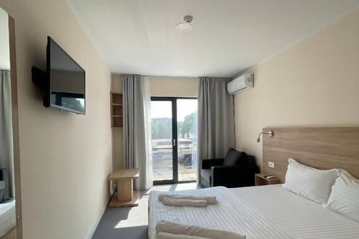 Ein Hotelzimmer mit einem großen Bett, einem flachbildfernseher an der Wand, einem Schreibtisch und einem Sessel.